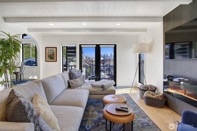 living room with wood finished floors, beamed ceiling, and a glass covered fireplace