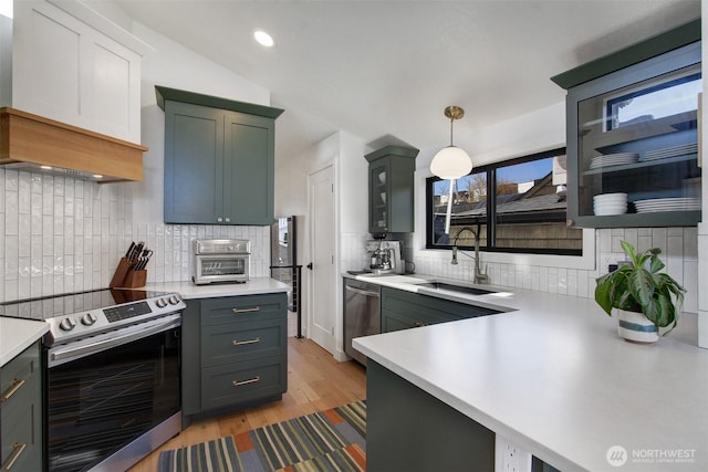 kitchen with stainless steel appliances, light countertops, light wood-style flooring, and a sink