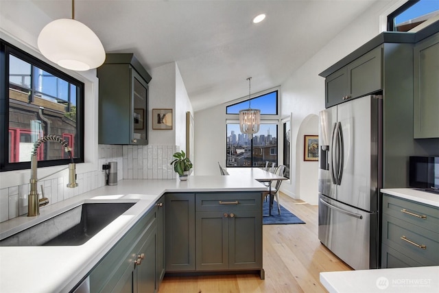 kitchen with lofted ceiling, a sink, an inviting chandelier, light wood finished floors, and stainless steel fridge with ice dispenser