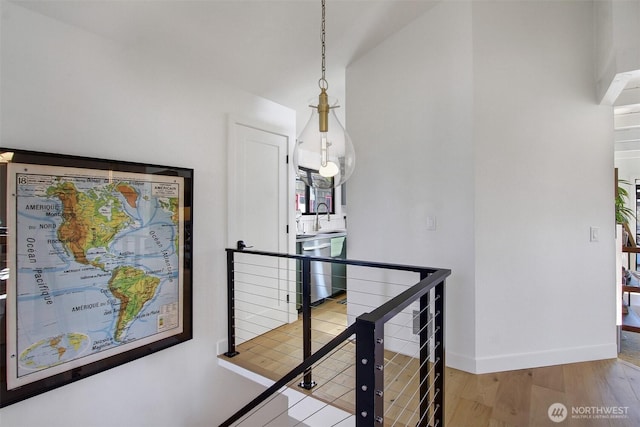 corridor with an upstairs landing, wood finished floors, baseboards, and a sink