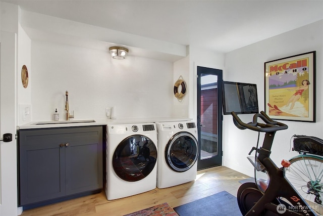 laundry area with cabinet space, a sink, light wood-style flooring, and washer and clothes dryer