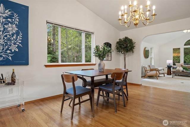 dining room with arched walkways, lofted ceiling, wood finished floors, and a notable chandelier