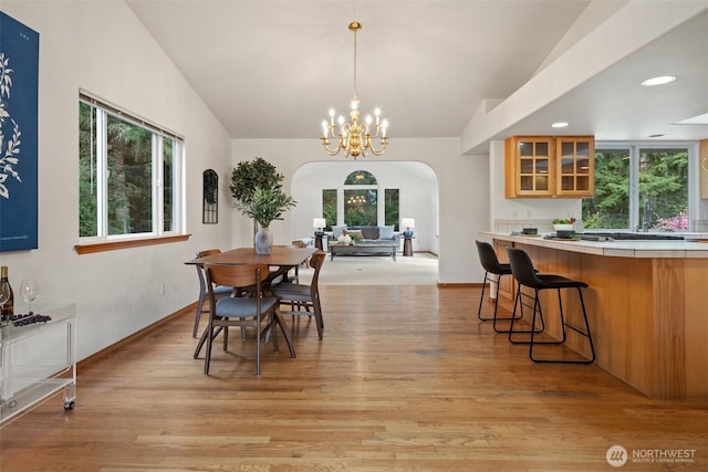 dining area with light wood finished floors, vaulted ceiling, arched walkways, and recessed lighting