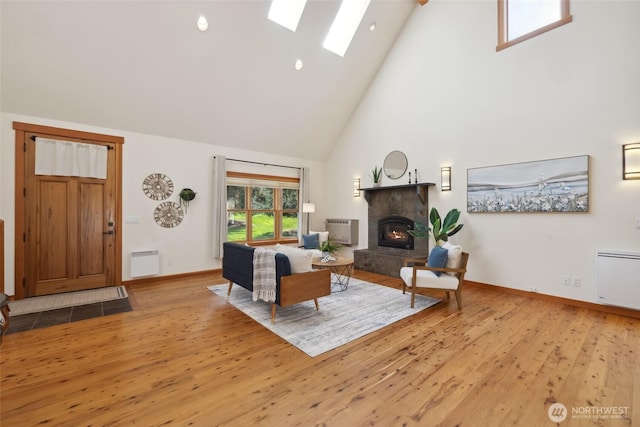 living room with baseboards, a skylight, wood finished floors, a stone fireplace, and high vaulted ceiling
