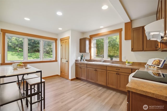 kitchen with recessed lighting, brown cabinetry, range hood, and a sink