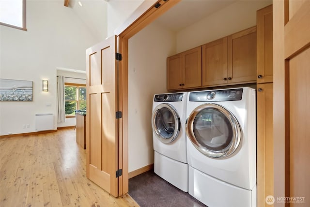 laundry room with a towering ceiling, washing machine and dryer, light wood-style floors, baseboards, and cabinet space