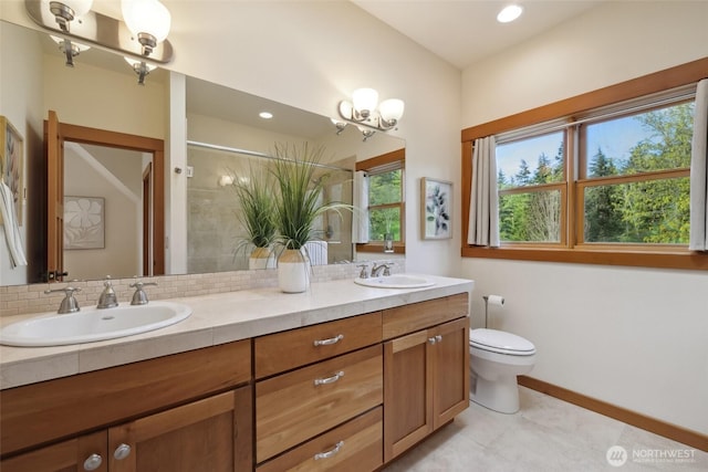 full bath with toilet, a sink, double vanity, and baseboards