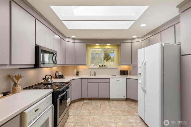 kitchen with a skylight, light countertops, gray cabinetry, and white appliances