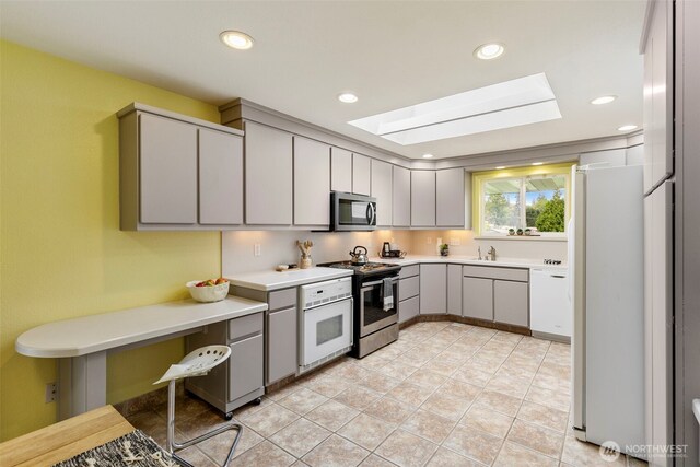 kitchen with light countertops, gray cabinets, a sink, a skylight, and stainless steel appliances