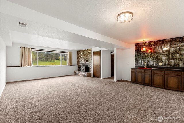 unfurnished living room with visible vents, a fireplace, light carpet, indoor wet bar, and a textured ceiling