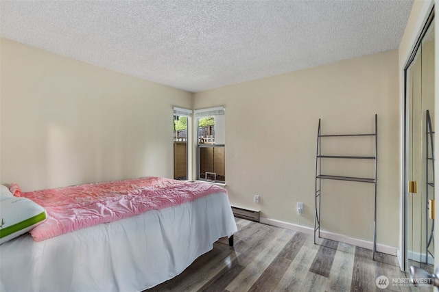 2534 S 317th St Unit 103, Federal Way, WA 98003 - bedroom with a baseboard heating unit, a closet, baseboards, a textured ceiling, and wood finished floors