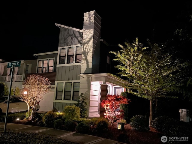 property exterior at night featuring a chimney and board and batten siding