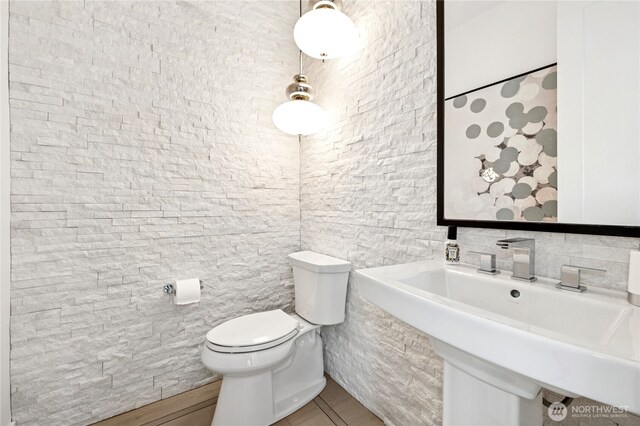 half bathroom featuring tile walls, tile patterned floors, toilet, and a sink