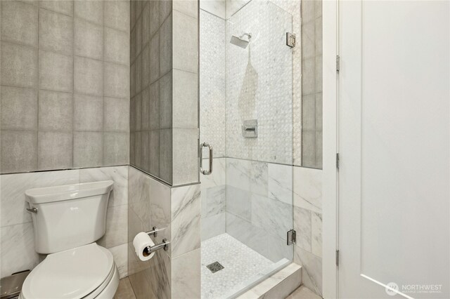 full bathroom featuring toilet, a stall shower, and tile walls