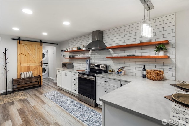 kitchen featuring stainless steel electric range oven, open shelves, stacked washer / drying machine, light countertops, and wall chimney exhaust hood