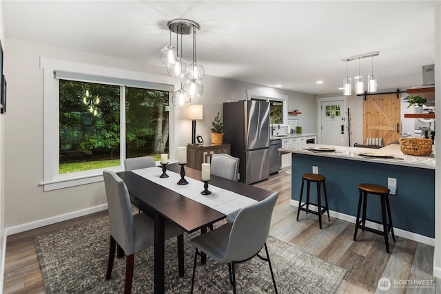 dining space featuring recessed lighting, a barn door, light wood finished floors, and baseboards