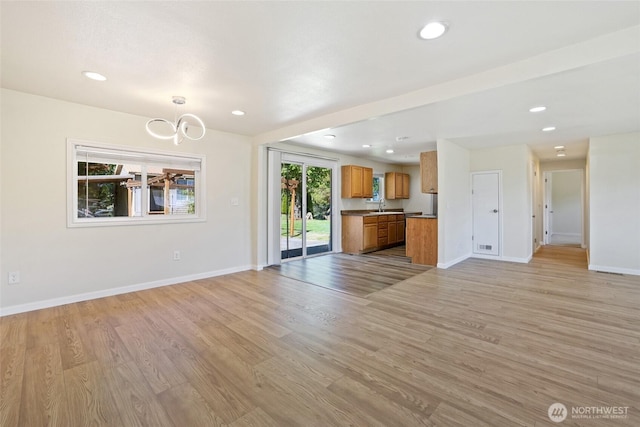 unfurnished living room with a sink, recessed lighting, baseboards, light wood-style flooring, and a chandelier