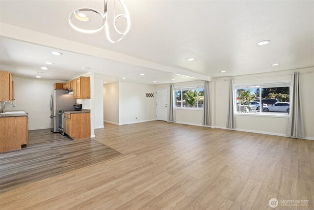 unfurnished living room with a sink, recessed lighting, light wood finished floors, and baseboards