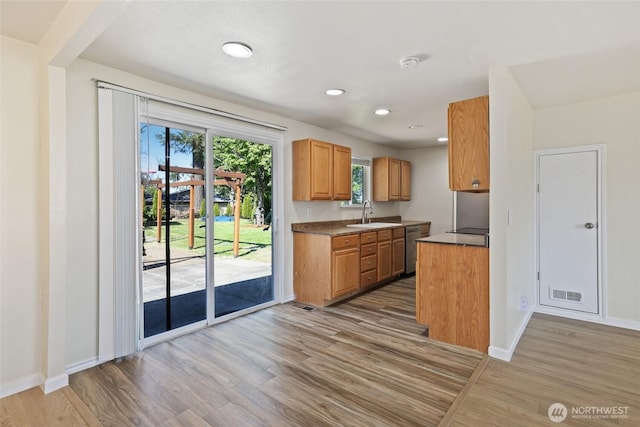 kitchen with light wood-style floors, stainless steel dishwasher, baseboards, brown cabinets, and a sink