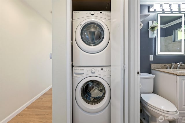 clothes washing area with stacked washer / drying machine, light wood-style flooring, and baseboards