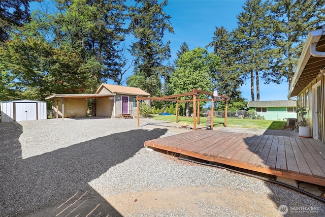 view of yard with a storage unit, an outbuilding, a wooden deck, fence, and a carport
