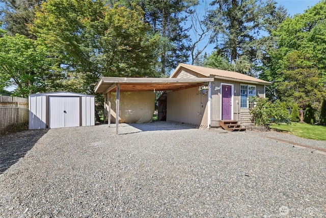 view of front of house featuring gravel driveway, a shed, fence, an outdoor structure, and an attached carport