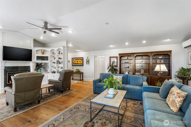 living room featuring ceiling fan, a premium fireplace, baseboards, wood finished floors, and vaulted ceiling