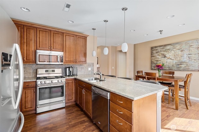 kitchen with light stone countertops, brown cabinets, dark wood-style flooring, a peninsula, and appliances with stainless steel finishes