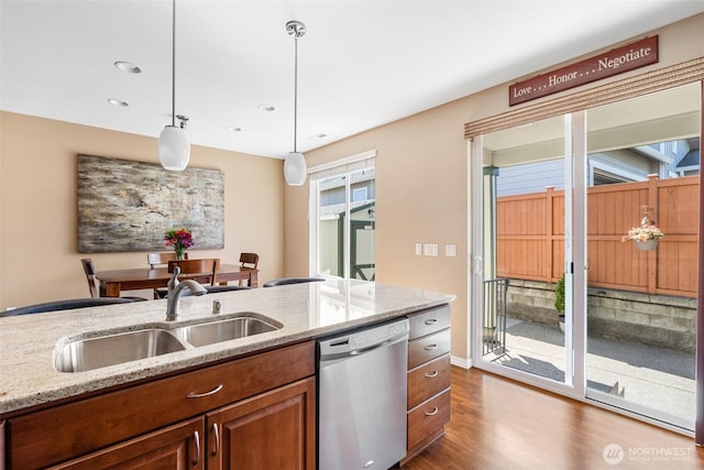 kitchen with dark wood-style floors, a sink, brown cabinets, stainless steel dishwasher, and hanging light fixtures