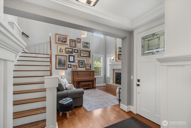 entrance foyer with a glass covered fireplace, baseboards, wood finished floors, stairway, and ornamental molding