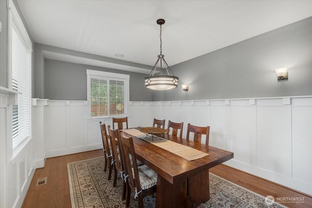dining room with wood finished floors, a decorative wall, a wainscoted wall, and visible vents