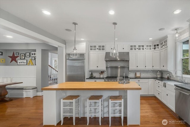 kitchen featuring a sink, white cabinetry, butcher block counters, under cabinet range hood, and appliances with stainless steel finishes
