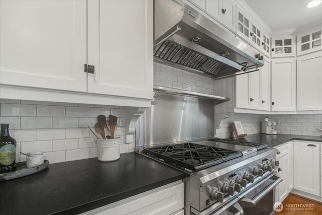 kitchen with white cabinets, under cabinet range hood, dark countertops, high end stainless steel range oven, and decorative backsplash