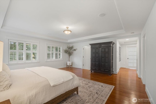bedroom featuring baseboards, wood finished floors, a tray ceiling, and crown molding