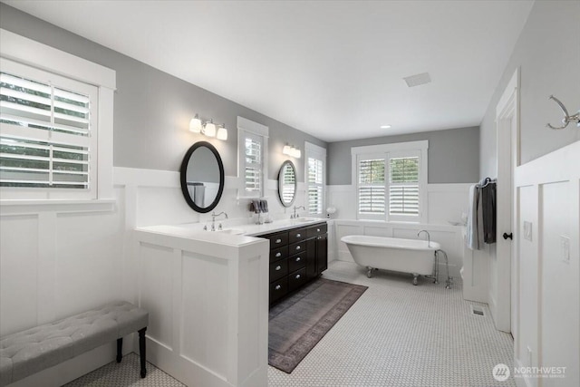 bathroom with a freestanding bath, double vanity, a wainscoted wall, and a sink