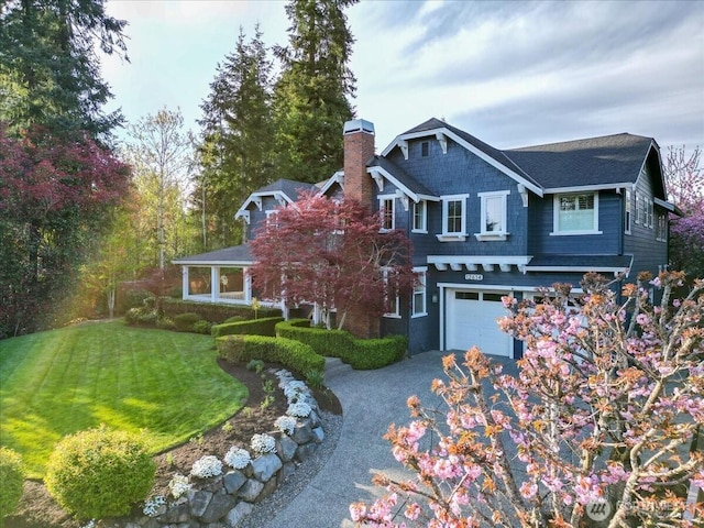 view of front of property featuring a chimney, a shingled roof, an attached garage, driveway, and a front yard