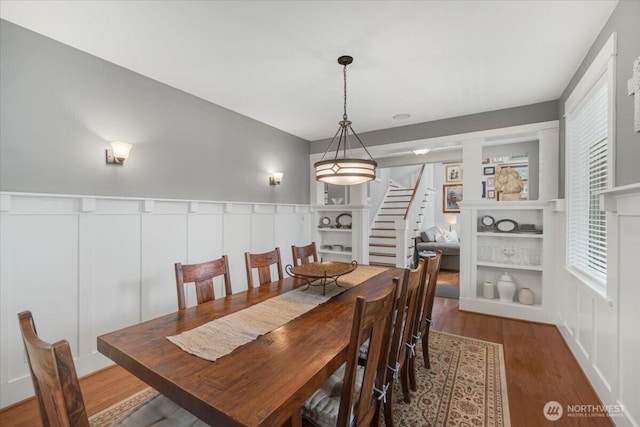 dining space with wainscoting, wood finished floors, stairway, and a decorative wall