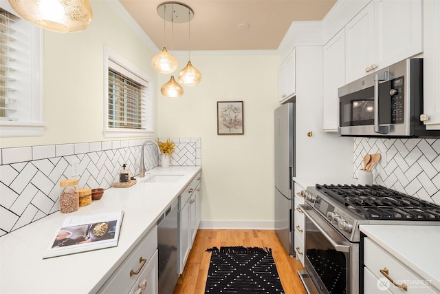 kitchen with white cabinets, stainless steel appliances, backsplash, a sink, and light wood-type flooring