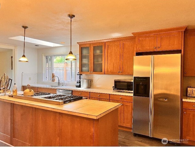 kitchen with a sink, a skylight, brown cabinetry, and stainless steel appliances