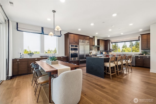13748 SE 84th St Unit 17, Newcastle, WA 98059 - kitchen with wall chimney exhaust hood, a center island, visible vents, dark brown cabinetry, and appliances with stainless steel finishes