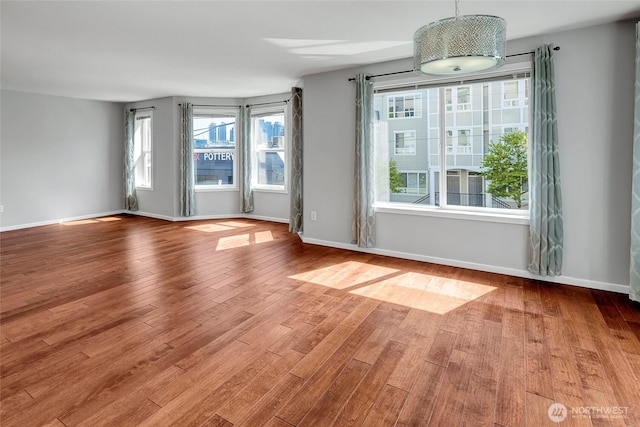 unfurnished room with a wealth of natural light, wood finished floors, and baseboards