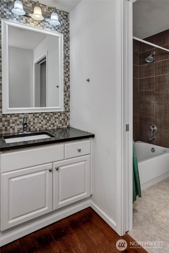 bathroom with bathtub / shower combination, decorative backsplash, baseboards, and vanity