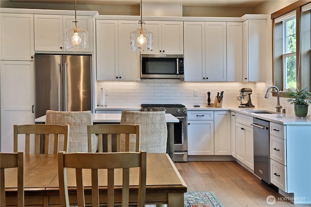 kitchen featuring decorative backsplash, hanging light fixtures, a sink, light wood finished floors, and stainless steel appliances