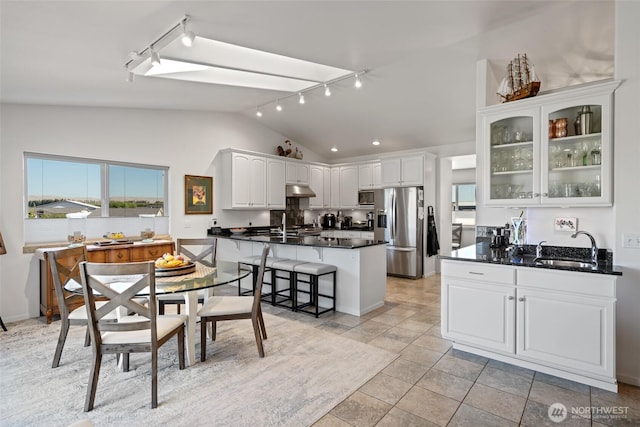kitchen with a sink, stainless steel appliances, rail lighting, vaulted ceiling, and dark countertops