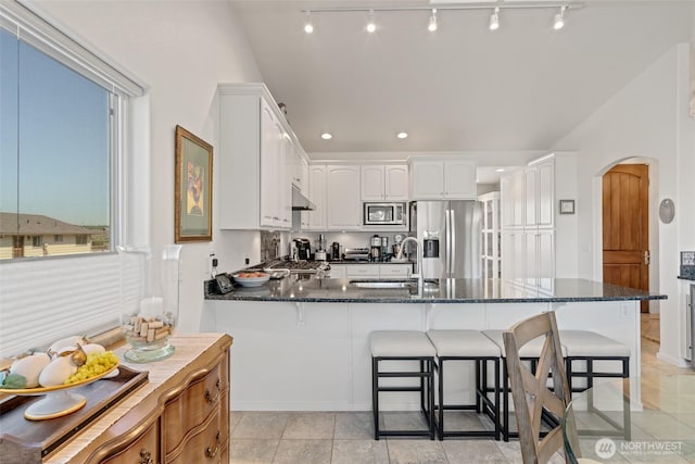 kitchen featuring a sink, appliances with stainless steel finishes, arched walkways, rail lighting, and a peninsula