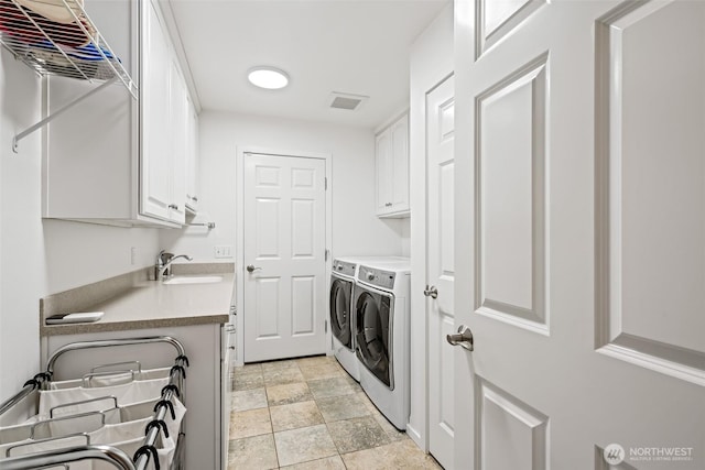 clothes washing area with a sink, cabinet space, washing machine and dryer, stone finish flooring, and visible vents