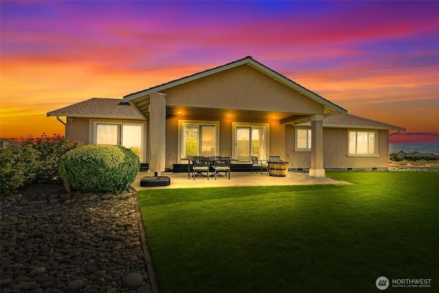 back of property at dusk featuring a patio, a yard, and stucco siding