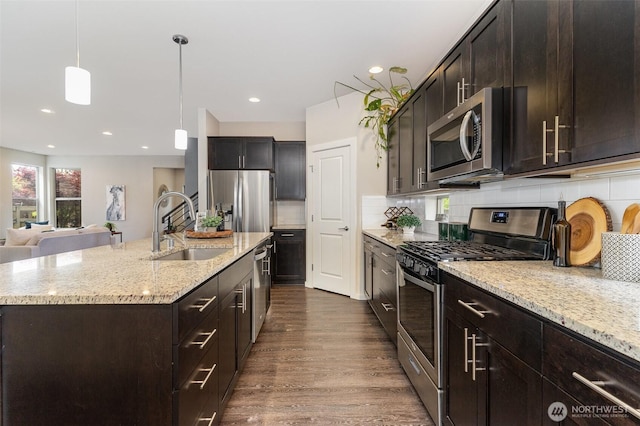 kitchen with stainless steel appliances, a sink, light stone counters, dark wood finished floors, and backsplash