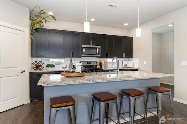 kitchen with stainless steel appliances, a sink, dark wood finished floors, a kitchen breakfast bar, and recessed lighting