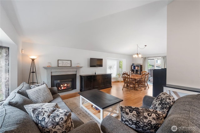 living room featuring light wood-type flooring, a glass covered fireplace, and a chandelier